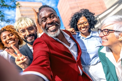 Lidé různého věku, ras a&nbsp;pohlaví se usmívají před budovou